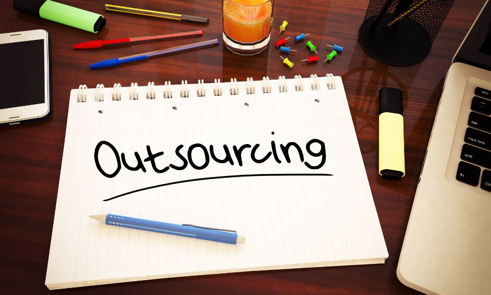 Outsourcing written on a notepad placed on a sales manager’s desk.