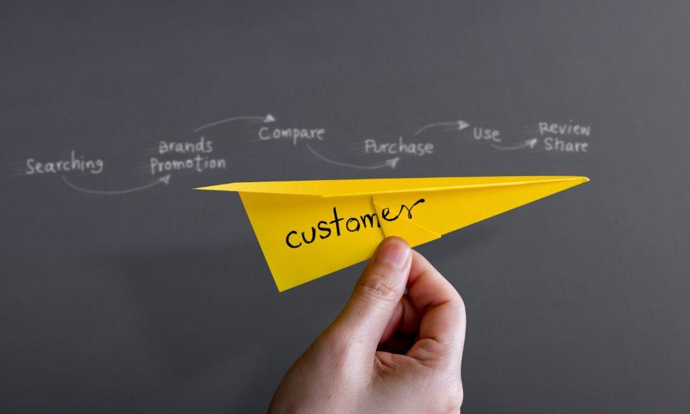 A person holding a paper plane in front of the customer journey stages written on a chalkboard.