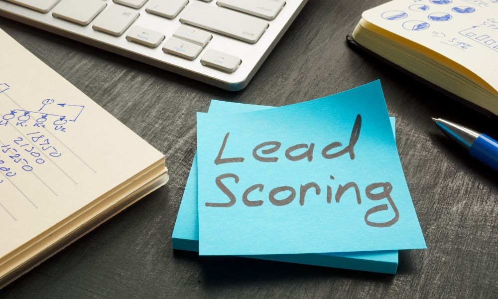 A memo with lead scoring written on it surrounded by a computer keyboard and notepads.