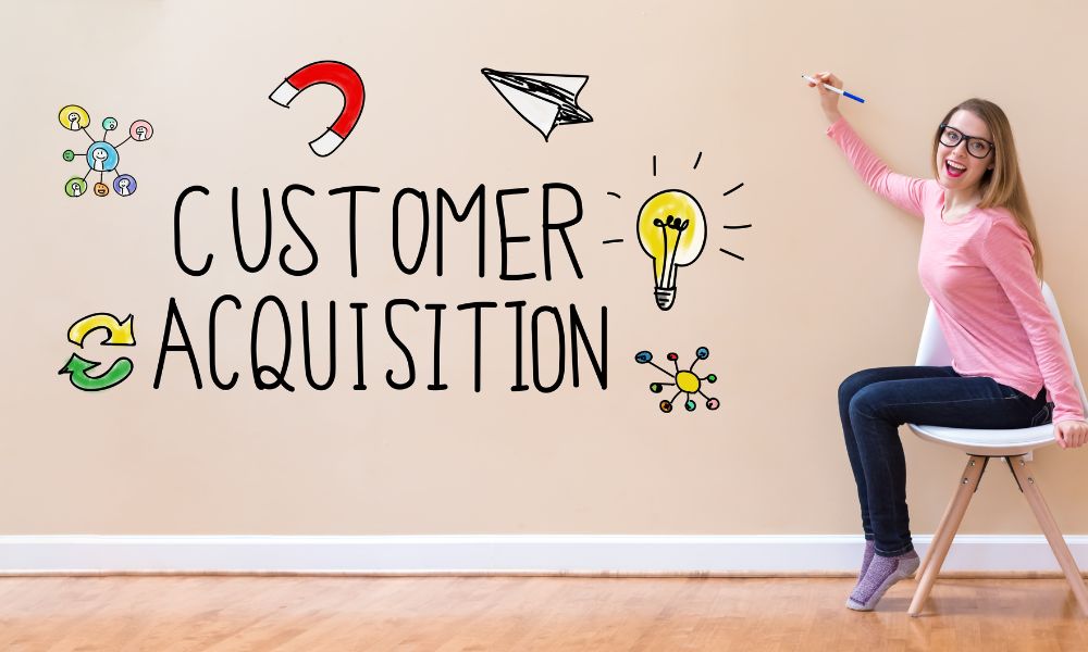 Woman holding a pen and the words Customer Acquisition written on a wall surrounded by related symbols.